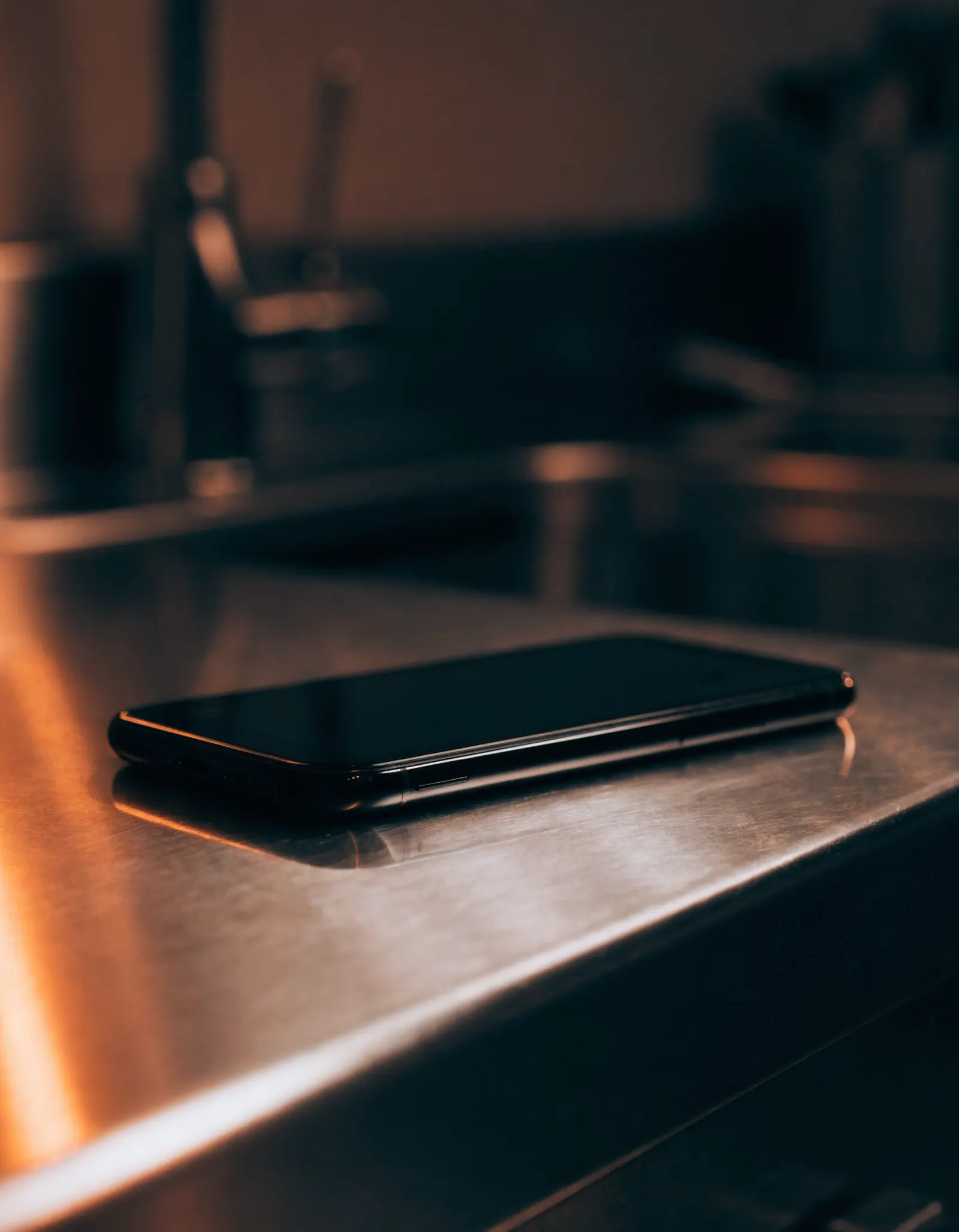 A phone lying face up on a stainless counter, screen dark